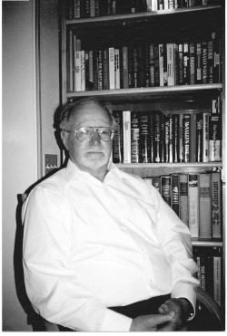 Photograph of Mark Perakh sitting in front of books